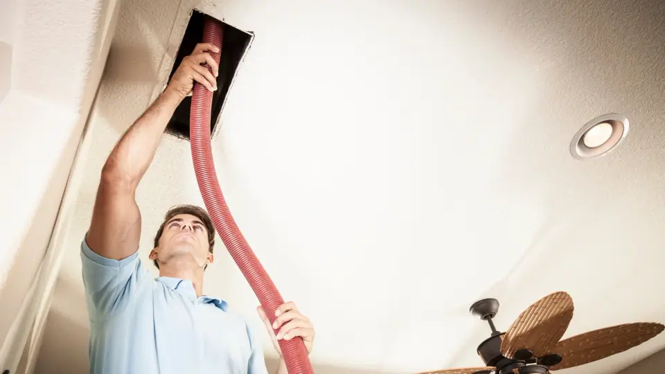 Technician cleaning a ceiling duct opening in a home